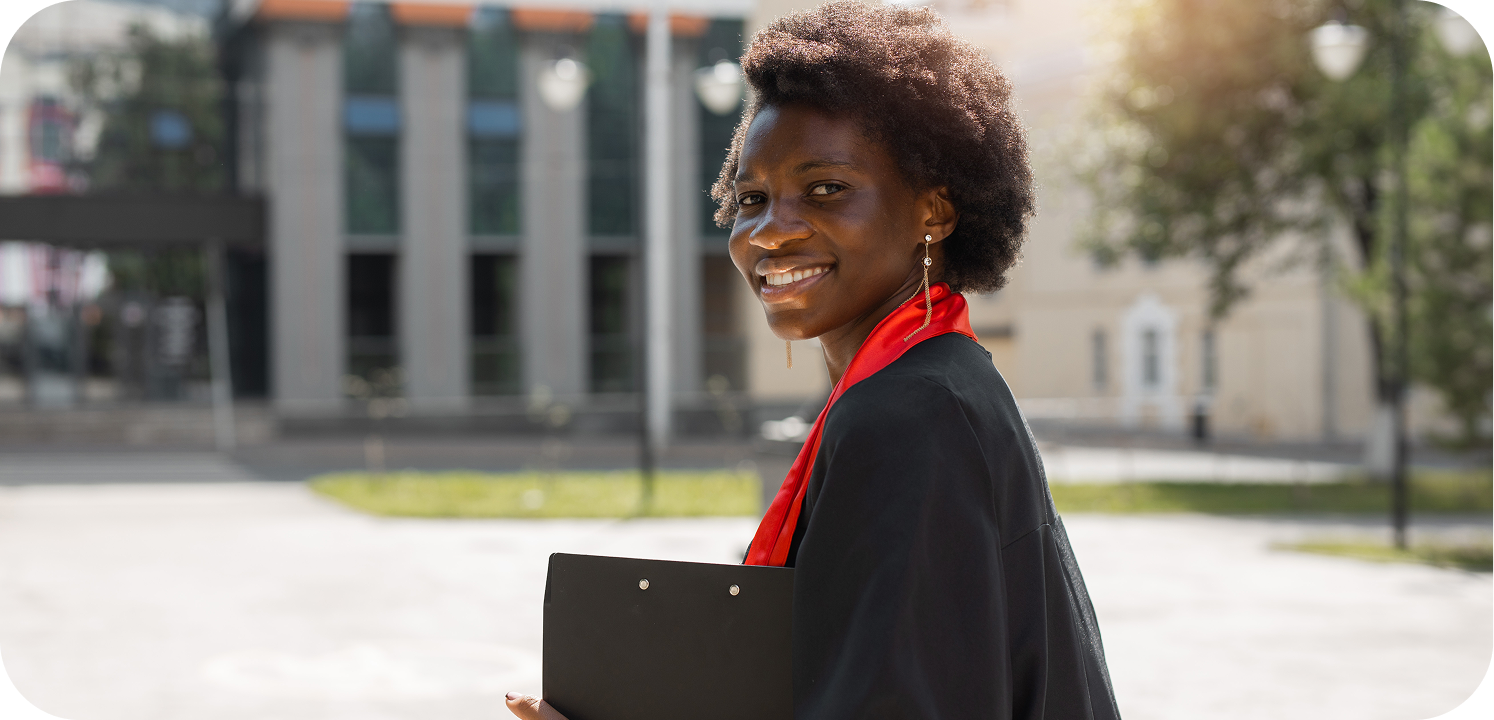 A smiling law student in graduation gown holding books outside campus